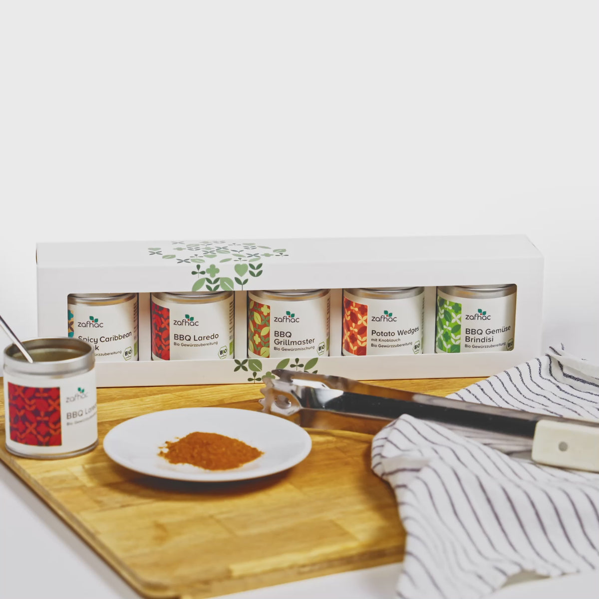 zafhac Geschenkset Grillmeister mit fünf Bio-Grillgewürzen, Grillzange und Gewürz auf einem Holzbrett.